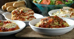 An assortment of pasta dishes, a fresh salad, and breadsticks displayed on a wooden table.